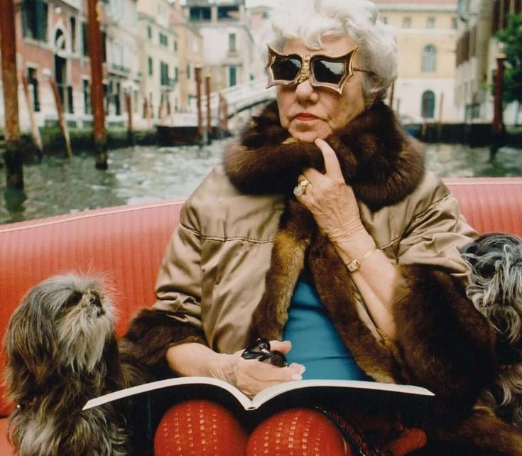 Woman in fur coat and sunglasses reading a book on a boat in Venice